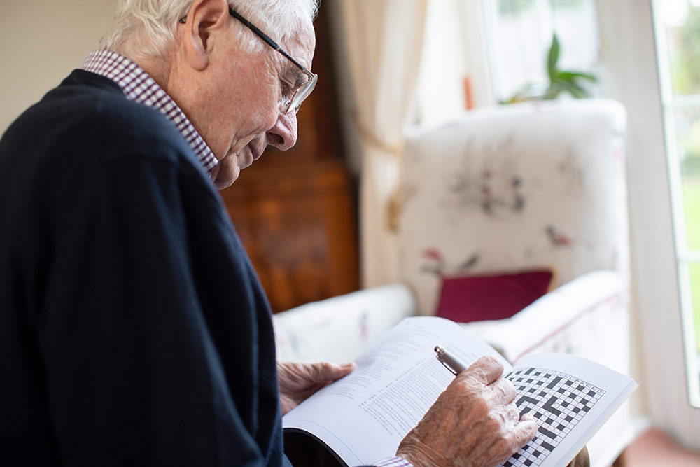 Senior man sitting in assisted living community doing crossword puzzle