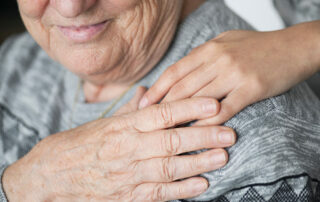 Close up of senior sitting down with hand on shoulder touching caregivers hand on shoulder