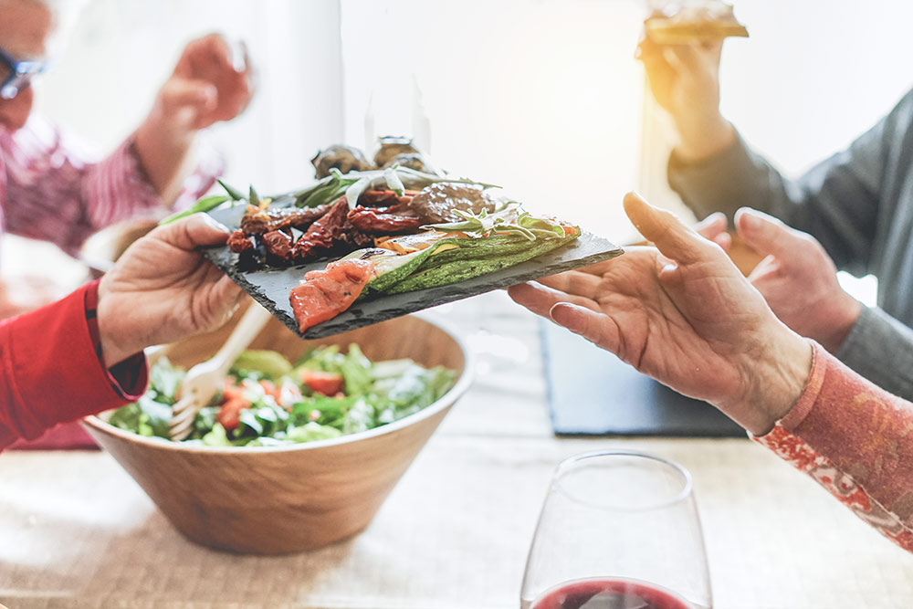 Seniors at dinner table passing plate of healthy food