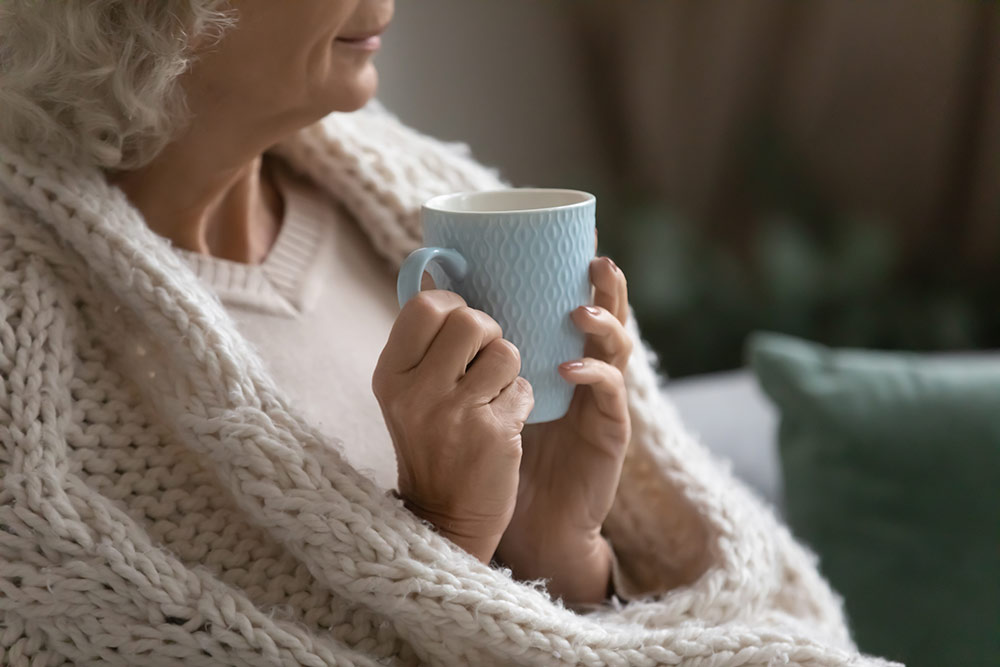 Close up of woman wrapped in blanket sitting on couch with cup of team in hands