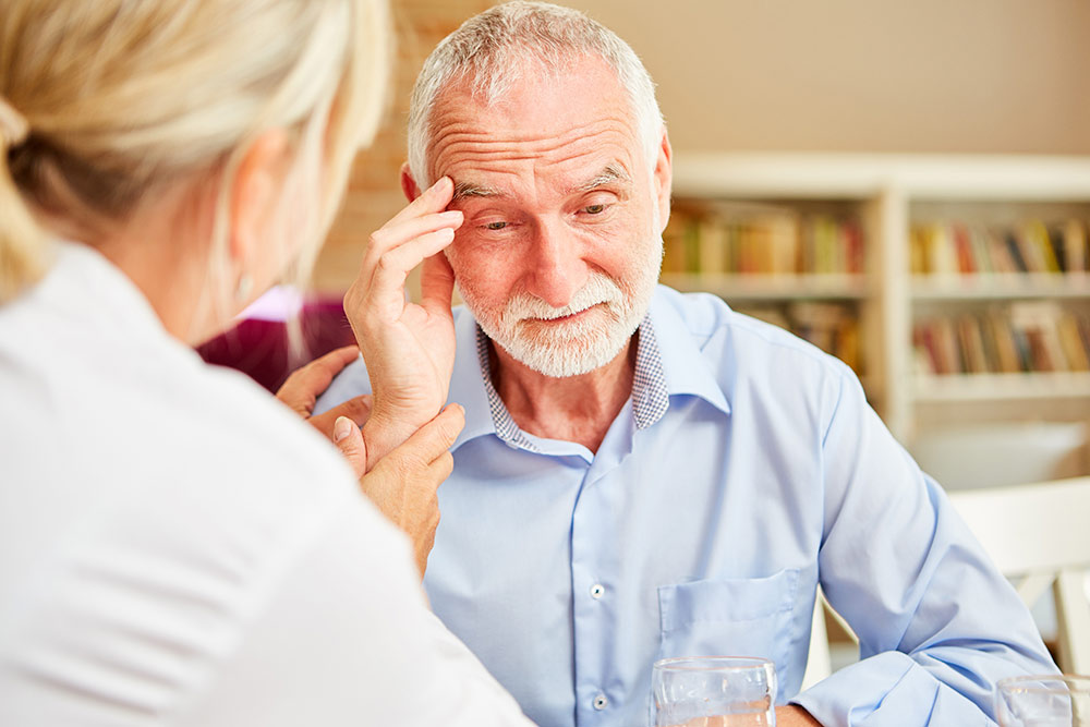 Senior man with dementia holding head with caregiver with him consoling him