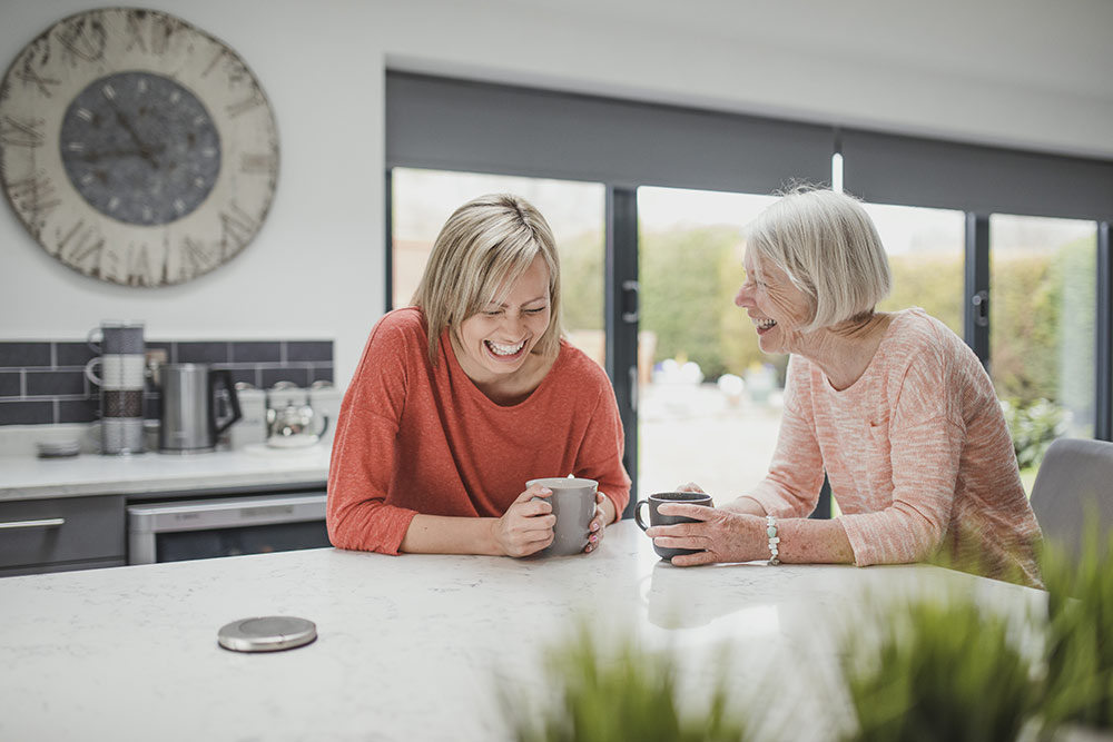 Two women laughing and drinking coffee in kitchen