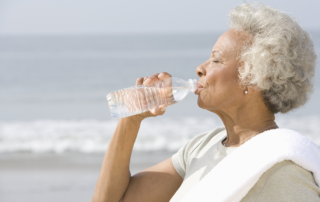 Senior woman outside by beach, drinking water