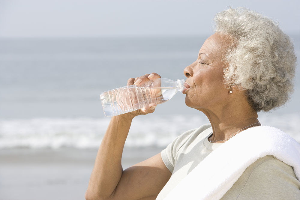 Senior woman outside by beach, drinking water