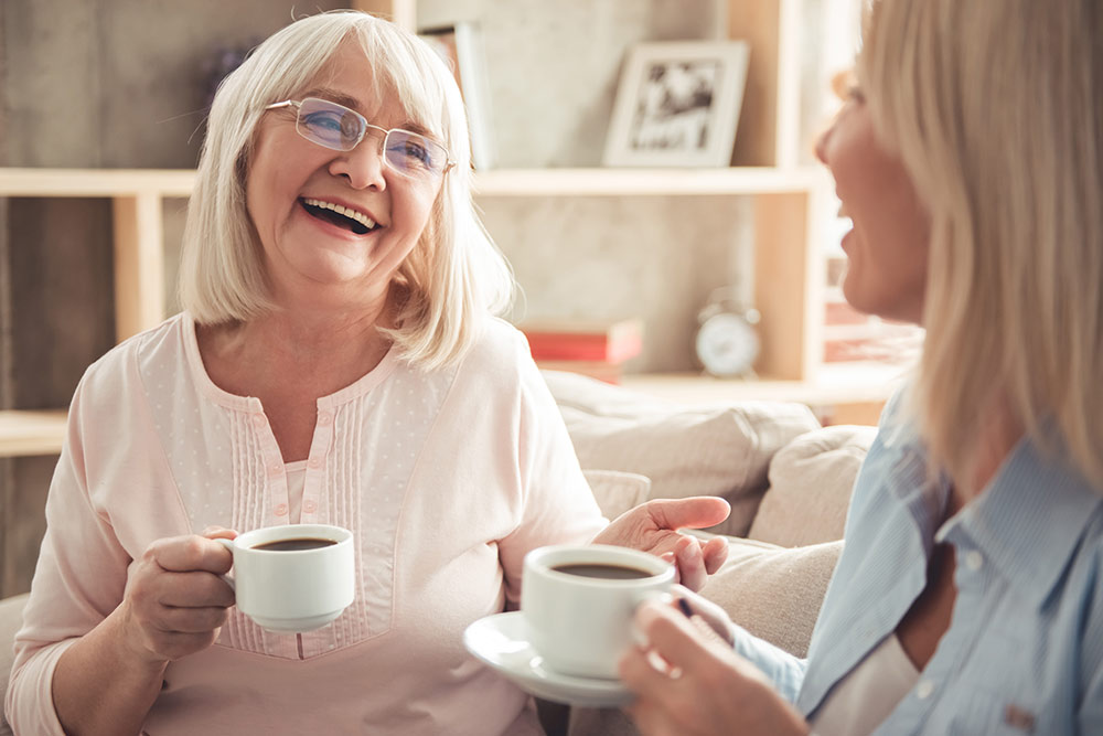 Happy senior women sitting down laughing and talking while drinking coffee