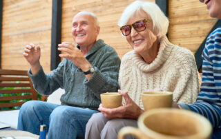 A group of senior friends drink tea outdoor on a patio at assisted living