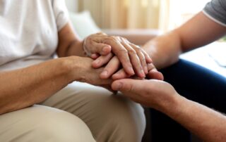 A caregiver and a senior woman hold hands