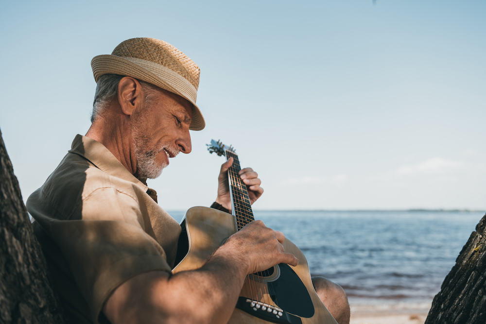A senior man plays the guitar by the ocean