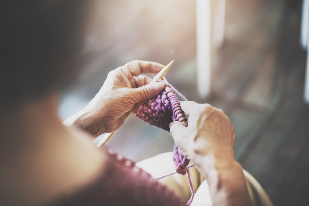 A senior woman works on knitting a sweater
