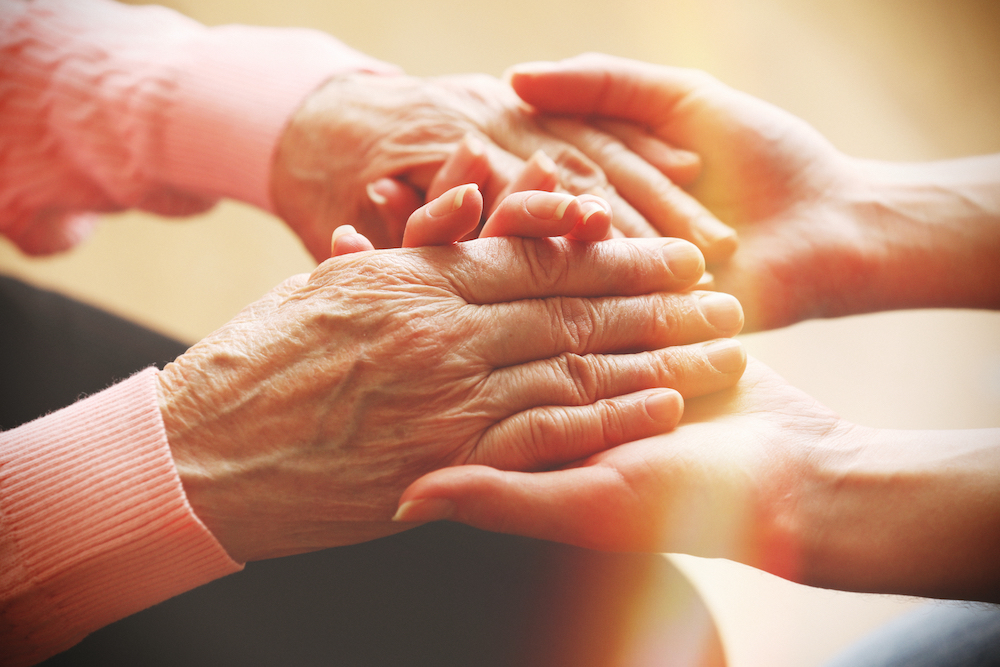 A senior woman holds hands with memory care services staff