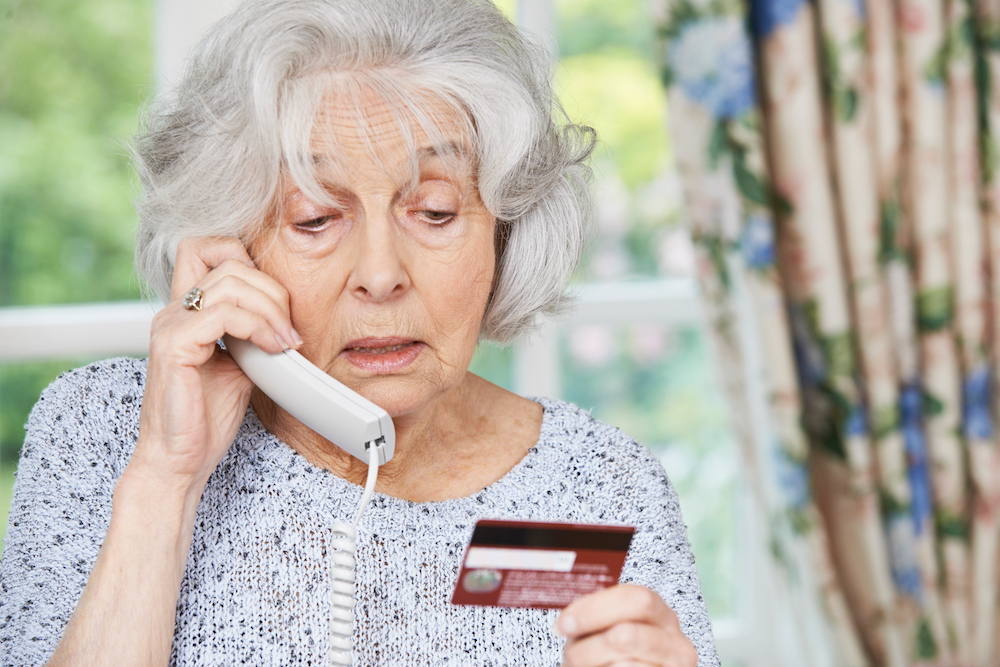 A concerned senior woman talking on the phone while holding her credit card