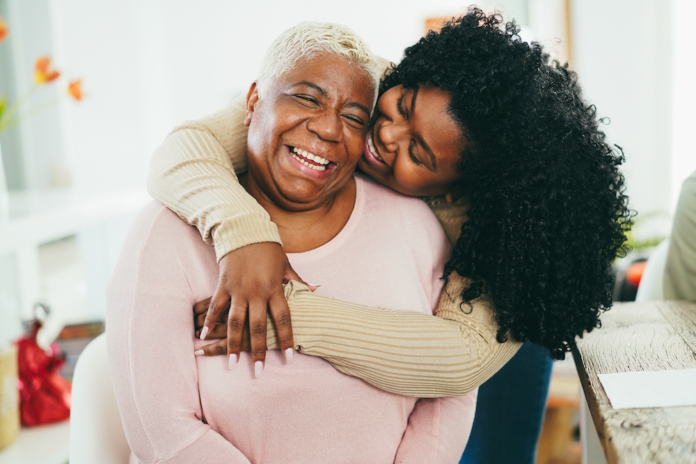 A young woman hugs her senior mother who uses memory care services