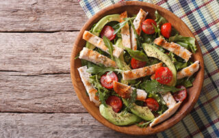 A healthy bowl of salad featuring chicken, tomatoes, and avocados