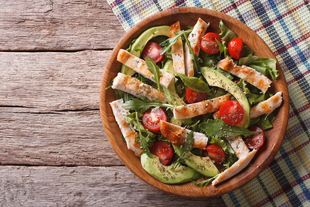 A healthy bowl of salad featuring chicken, tomatoes, and avocados