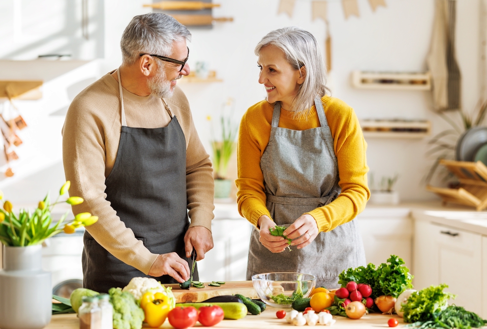 A senior couple cutting up veggies together in the kitchen