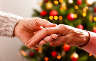 A senior woman and caregiver holding hands in front of holiday decorations