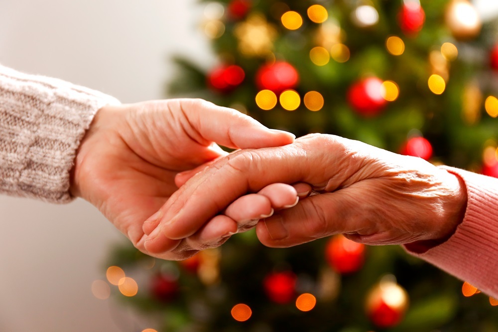 A senior woman and caregiver holding hands in front of holiday decorations