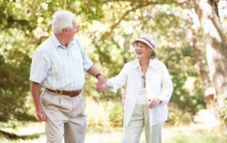 A laughing and happy senior couple go for a walk outdoors. Both receive memory care services from Bayshire Carlsbad