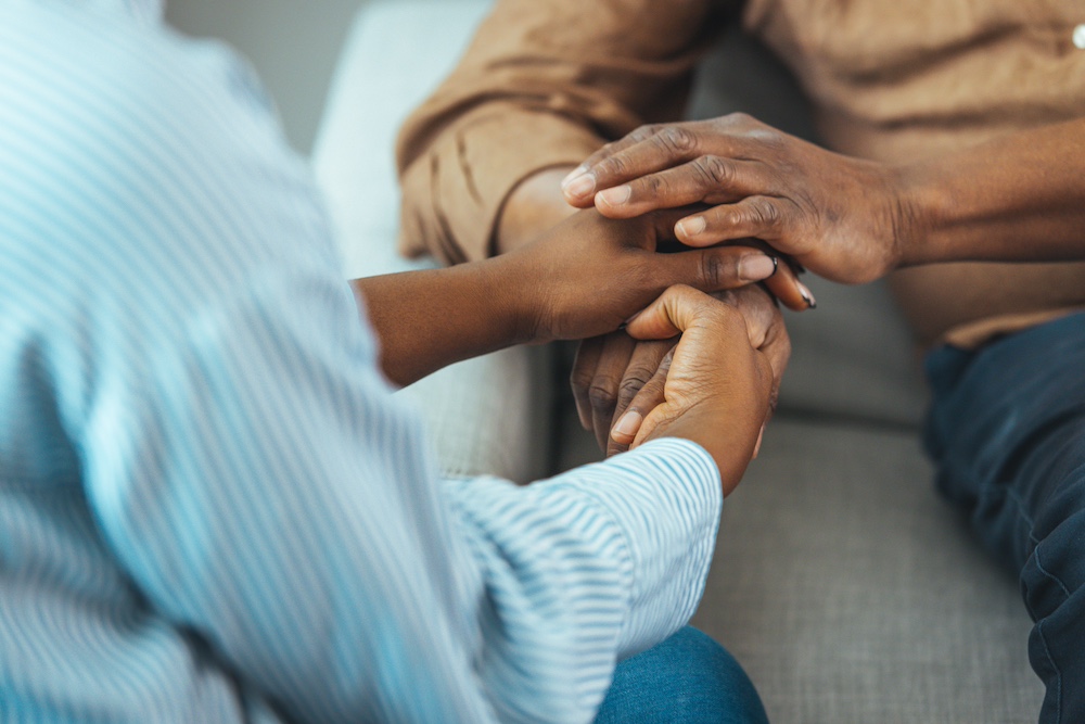 A senior man holding hands with his adult daughter as they discuss memory care services