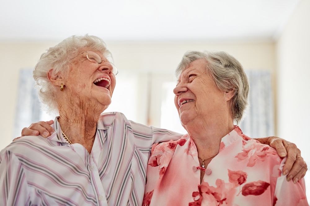 Two senior women laughing and enjoying memory care services at Bayshire Carlsbad